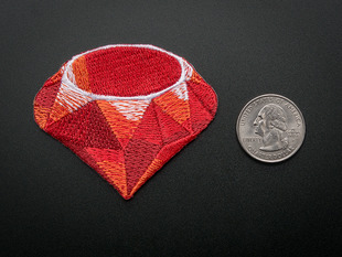 Embroidered trianglesque shaped badged of ruby programming logo, in red, with pink and white highlights. Next to a quarter for scale. 