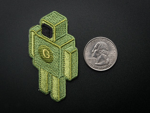 Embroidered, boxy robot shaped badge in green with black screen face and yellow G on chest. Shown next to a quarter for scale. 
