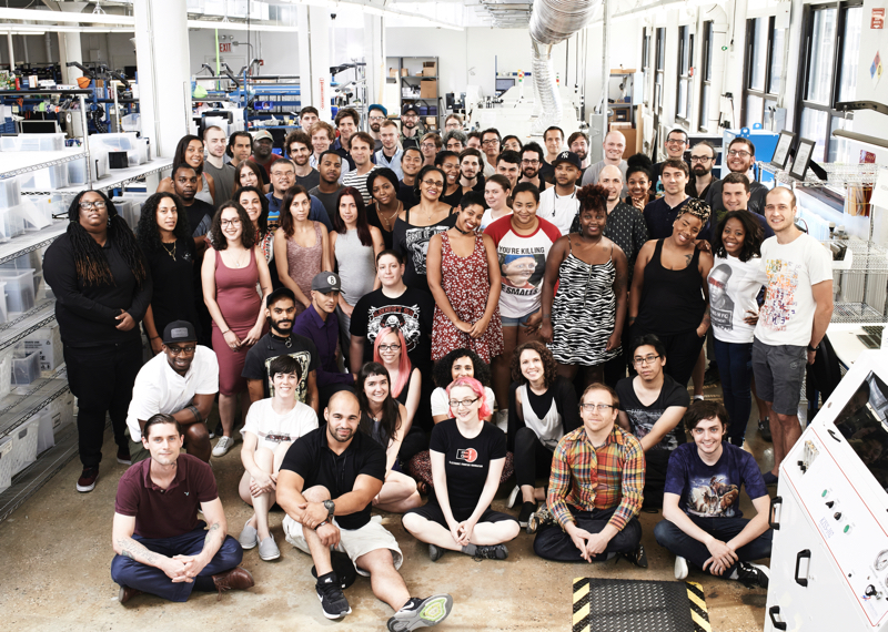Group photo of approximately 50 people in front of manufacturing equipment