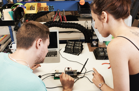 Two young individuals, backs turned, looking at electronic assembly on a worktable