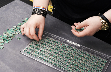 Two hands with punk bracelets assembling a grid of small electronic boards