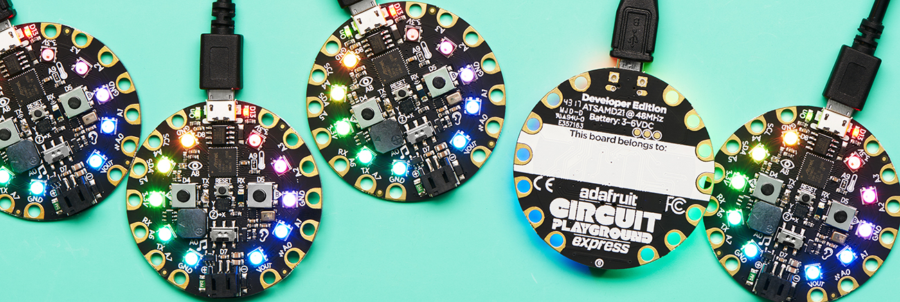 Five round circuit boards in a row, with rainbow LEDs, one is upside down and says Circuit Playground on back