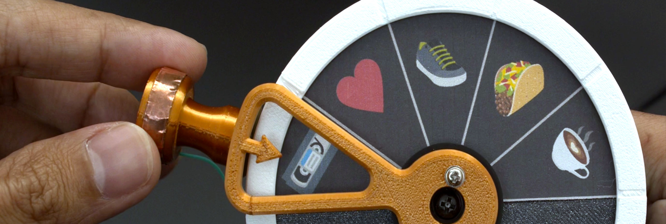a hand holding a 3d printed lever with images of a cassette tape, heart, shoe, taco, and coffee. 